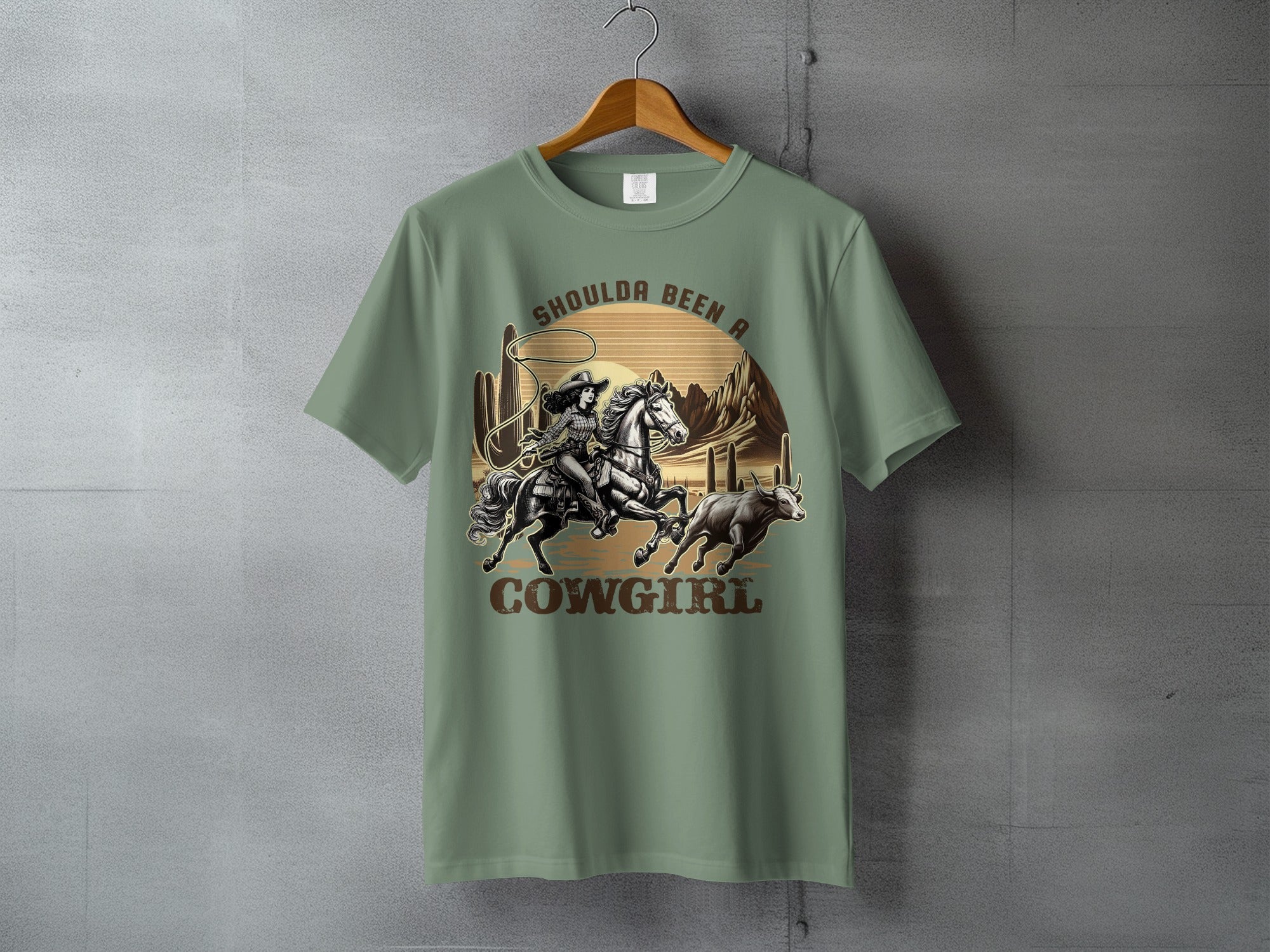 T-shirt graphic of a cowgirl riding a horse, roping a bull in a desert landscape.
