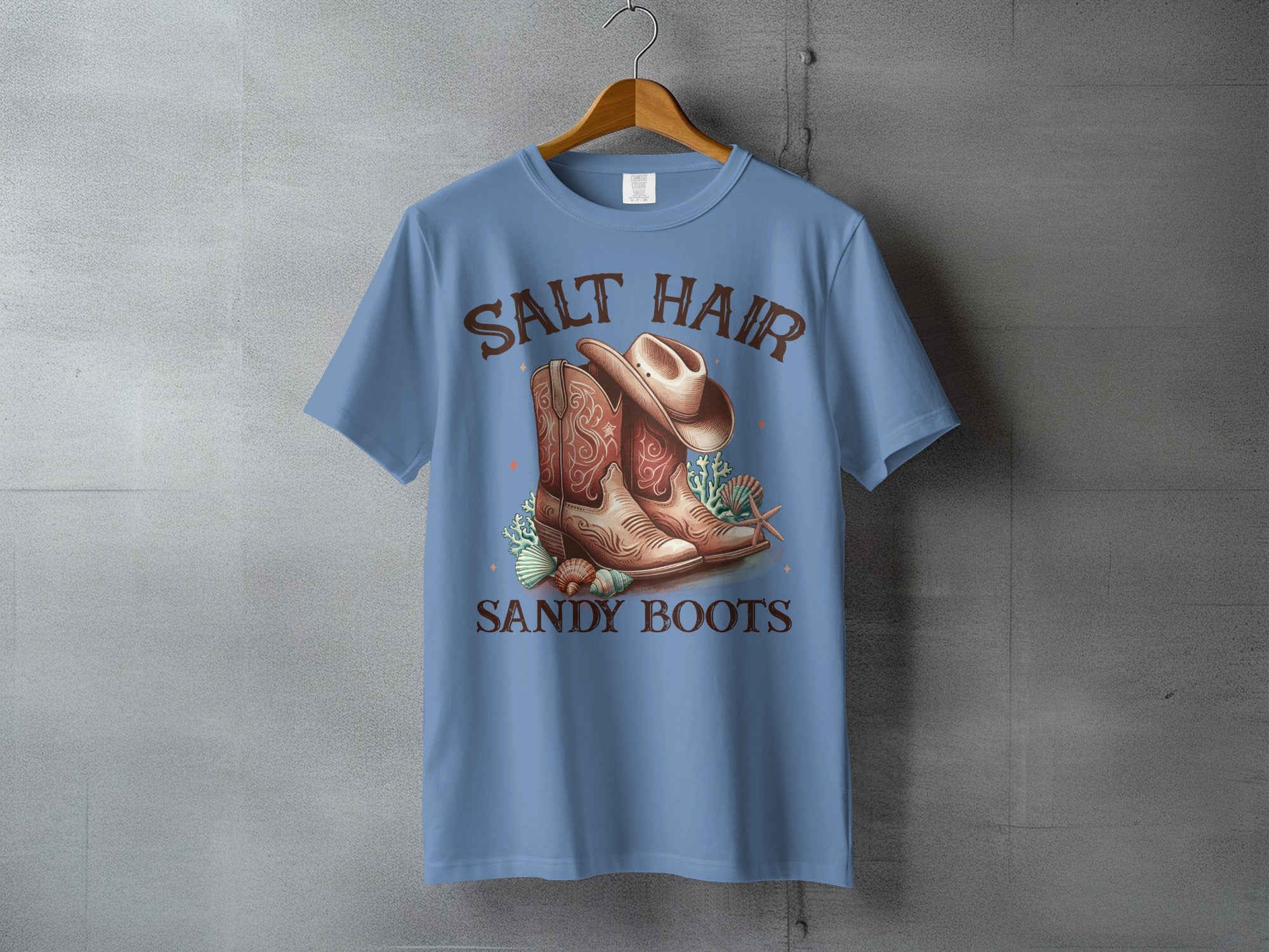 Blue t-shirt with cowboy boots, hat, and seashells graphic reading "Salt Hair Sandy Boots".