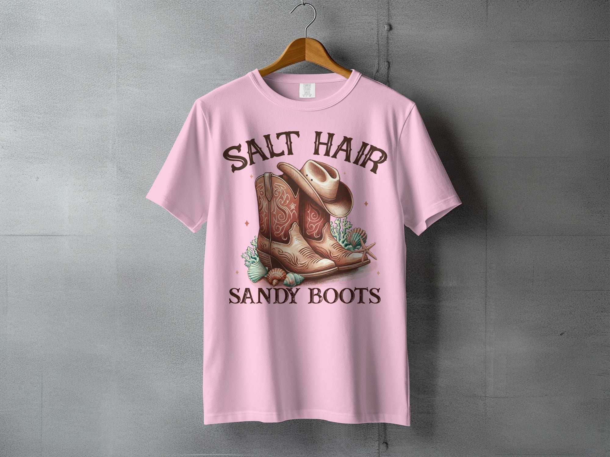 Pink t-shirt with cowboy boots, hat, and seashells, text reads SALT HAIR SANDY BOOTS.