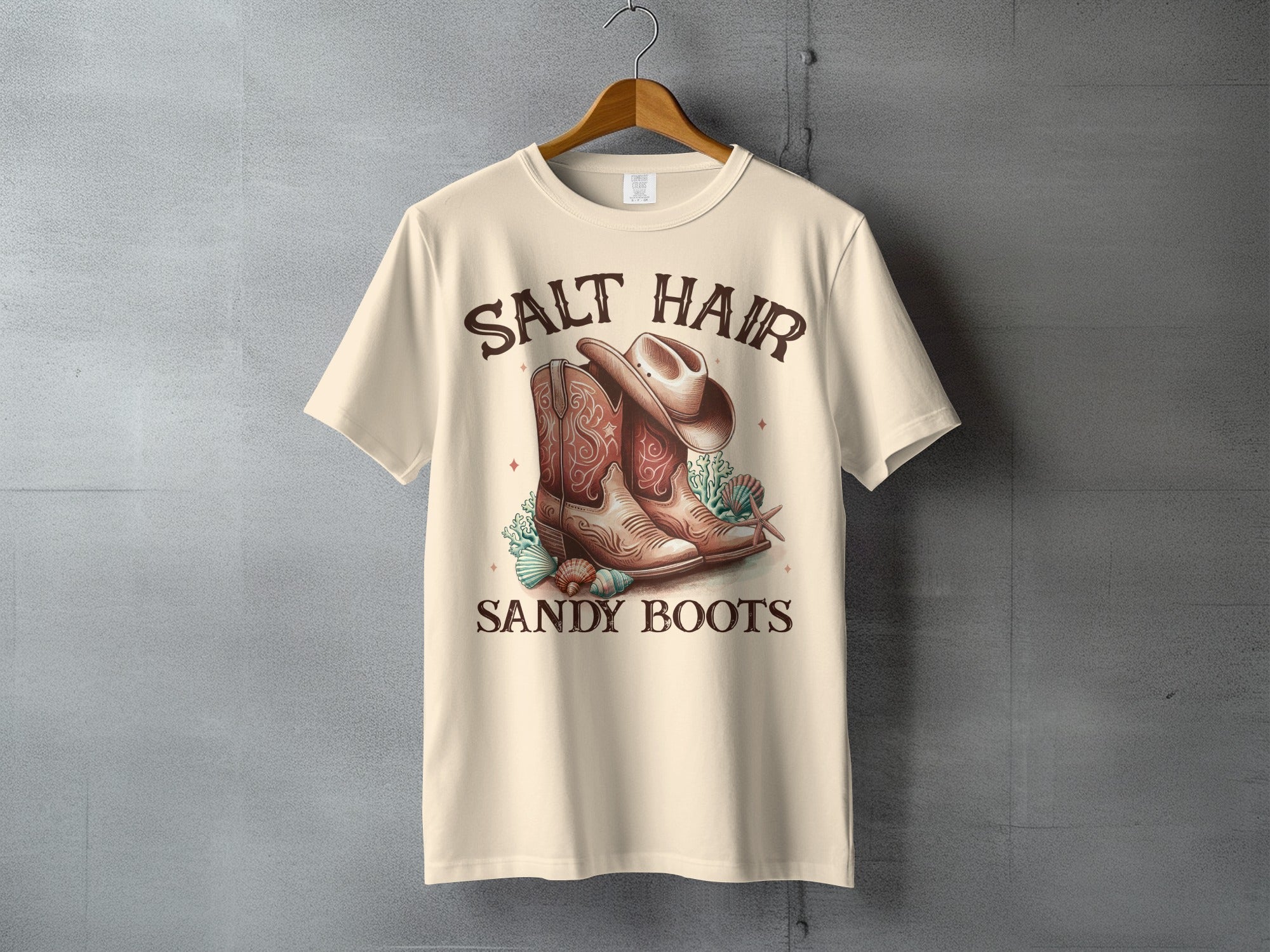 Cream t-shirt with "SALT HAIR SANDY BOOTS" text and cowboy boots, hat, and shells graphic.