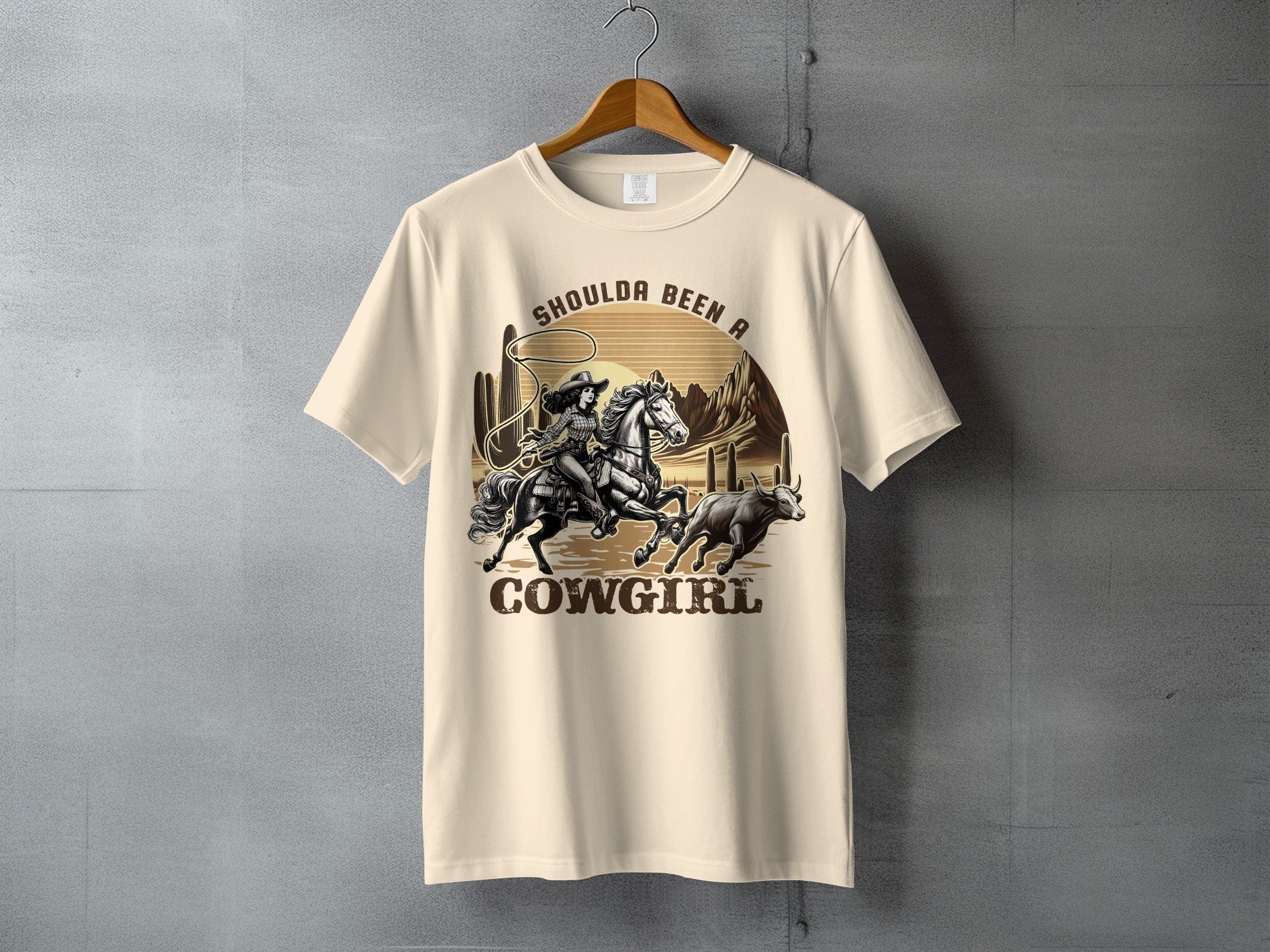 Cream t-shirt with illustration of cowgirl riding horse, lassoing a bull.